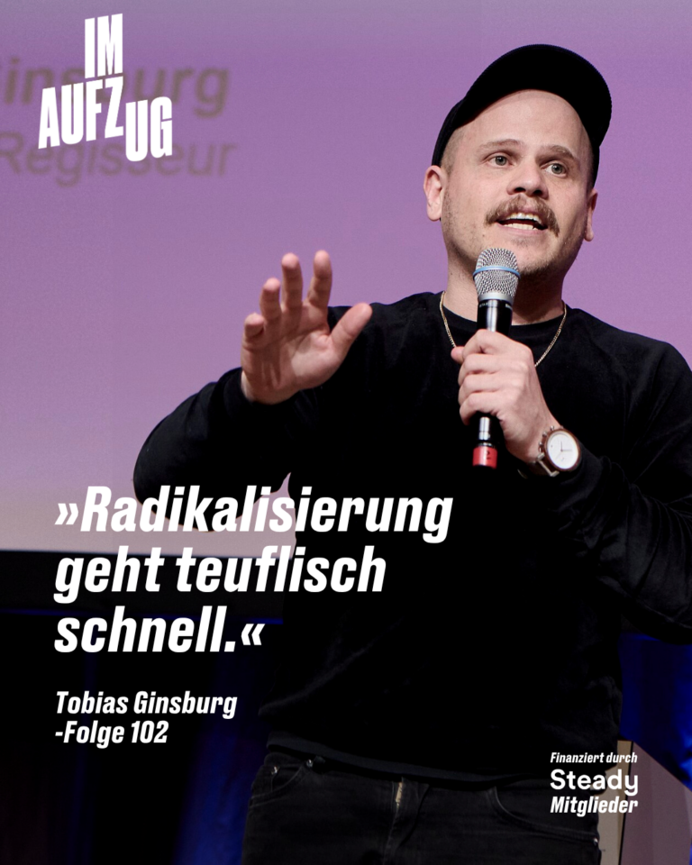 Foto von Tobias Ginsburg bei einem Bühnenauftritt. Er trägt ein schwarzes Langarmshirt, eine schwarze Kappe und eine Halskette, hält ein Mikrofon in der linken Hand und gestikuliert mit der rechten. Im Hintergrund ist eine lila beleuchtete Leinwand zu sehen, auf der sein Name und „Regisseur" steht. Oben links das Logo des Podcasts „Im Aufzug". Im unteren Bildbereich steht in großer weißer Schrift das Zitat: „Radikalisierung geht teuflisch schnell." Darunter: „Tobias Ginsburg – Folge 102". Unten rechts der Hinweis „Finanziert durch Steady Mitglieder".